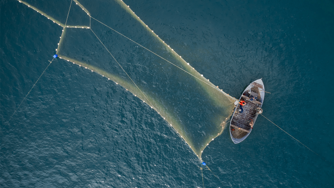 Boat drone photo. A fisherman on a fishing boat is casting a net for catching fish.